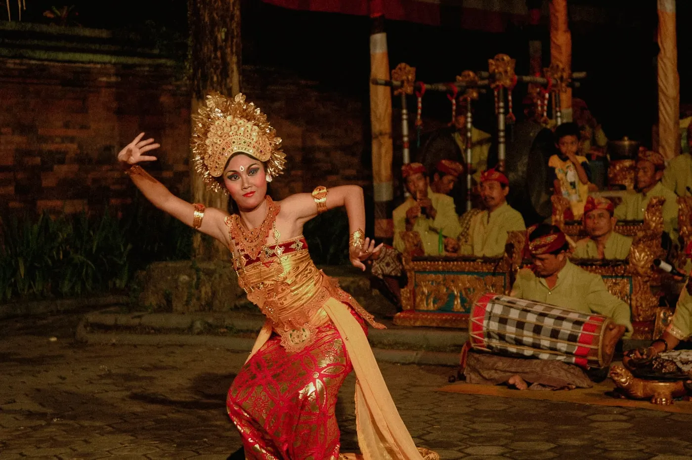 A Balinese dancer in gold headdress performing with the gamelan orchestra behind