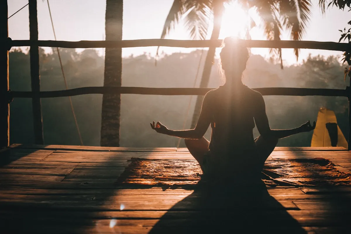 A person sitting in a yoga posture on an open deck at sunrise